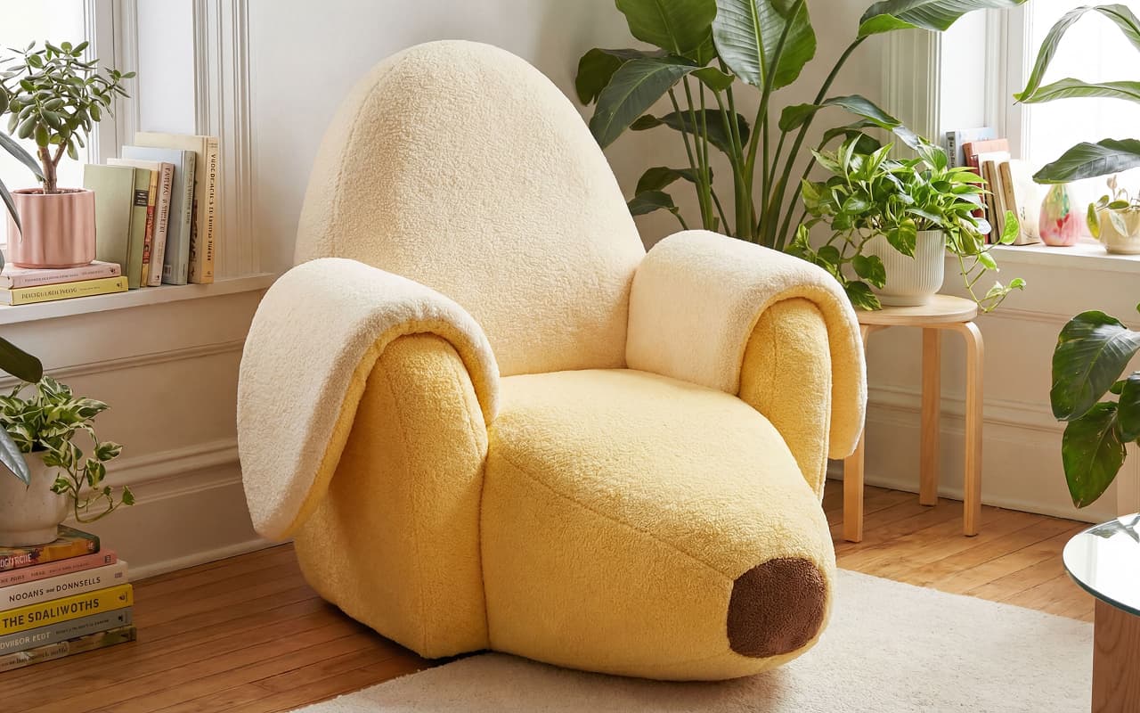 A soft yellow armchair shaped like a peeled banana in a bright, plant-filled room